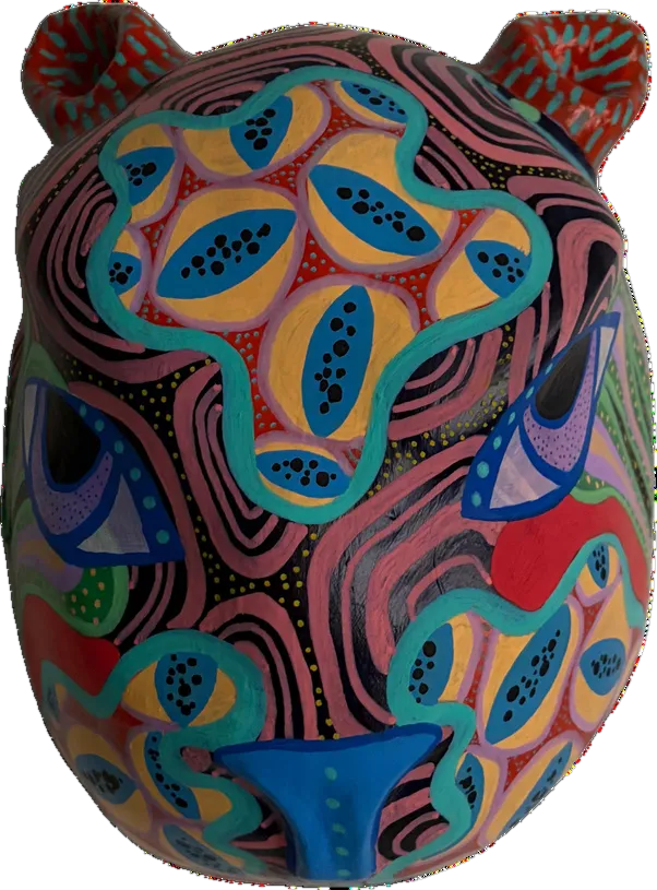 Máscara con forma de felino pintada en tonos tierra y rosa, con hojas y ojos ovalados en azul y turquesa recorriendo su volumen.